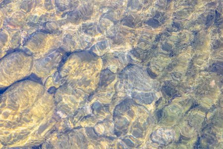 Natürliche Textur in der Natur mit einem natürlichen Muster von Wasserwellen und Steinen am Boden.