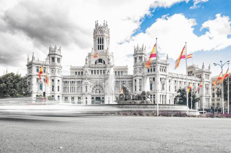 Timelapse at statue in the Plaza de Cibeles with the representation of the goddess of the same name and two lions with Spanish flags waving in the wind behind and traffic