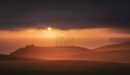 Photo for Dramatic skies and sunset behind Belle Tout lighthouse from the cliff edge of Beachy Head on the south downs east Sussex coast south east England UK - Royalty Free Image