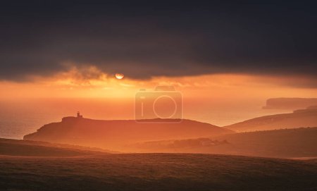 Photo for Dramatic skies and sunset behind Belle Tout lighthouse from the cliff edge of Beachy Head on the south downs east Sussex coast south east England UK - Royalty Free Image