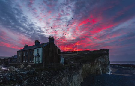 Photo for Dramatic dawn sky over the precarious cottages on the cliff edge of Birling Gap on the south downs east Sussex coast south east England UK - Royalty Free Image