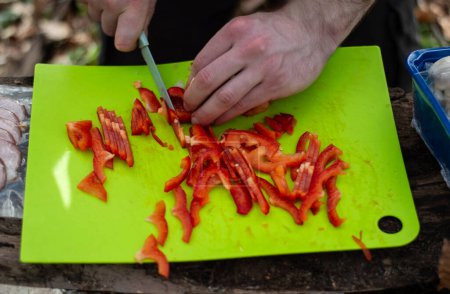 Cutting red paprika on a green cutting board in the forest
