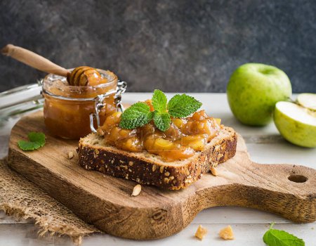Téléchargez les photos : Toast artisanal multi-grains avec conservation des pommes et menthe fraîche sur un panneau en bois sculpté - en image libre de droit