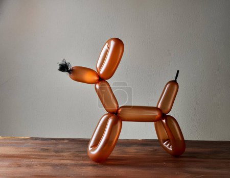 An orange balloon twisted into the shape of a playful dog against a white background