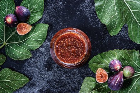 Photo for Figs homemade marmalade jar with fig leaves and fig fruits on dark background. Overhead view. - Royalty Free Image