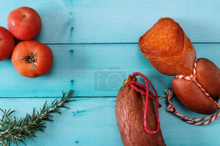 Foto de Productos alimenticios de Mallorca, salchichas sobrasadas, tomates y hierbas de romero sobre una mesa de madera azulada. Ángulo de vista - Imagen libre de derechos
