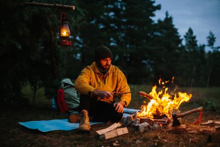 A lonely wanderer is having dinner in the mountains by a campfire.