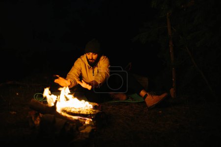 Photo for The traveler rests by the night campfire. Furnished shelter from branches for sleeping with a kerosene lamp and a fire surrounded by stones. - Royalty Free Image