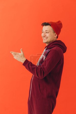 Photo for A young man in a Christmas kigurumi and a knitted hat on a colored background - Royalty Free Image