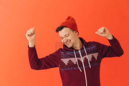 Photo for A young man in a Christmas kigurumi and a knitted hat on a colored background - Royalty Free Image