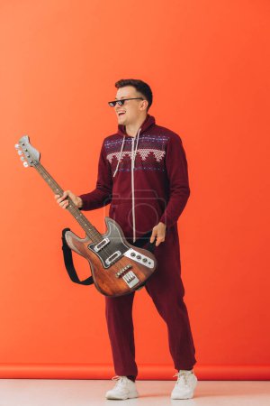 Téléchargez les photos : Un jeune homme dans un kigurumi de Noël joue de la guitare électrique sur un fond coloré. - en image libre de droit