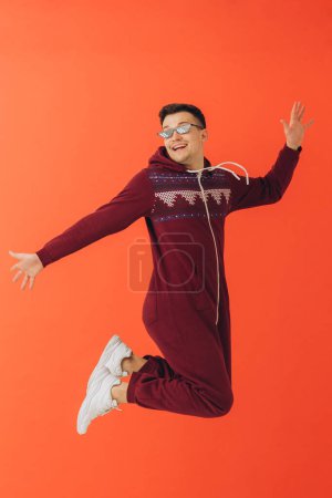 Photo for A young man in sunglasses and a Christmas kigurumi dances on a red background. - Royalty Free Image