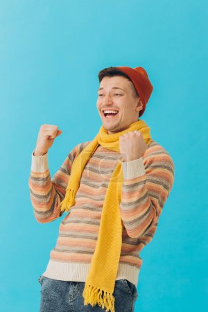 Photo for Handsome young man in winter clothes on color background. The winner's gesture - Royalty Free Image