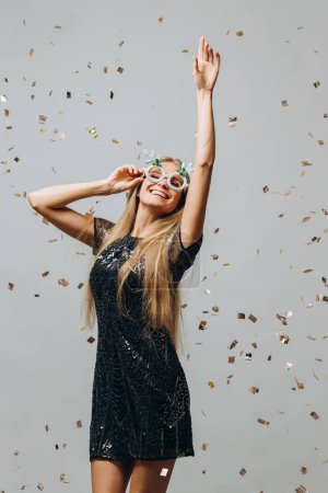 Photo for A beautiful blonde girl is dancing under glittering confetti. New Year party concept. - Royalty Free Image
