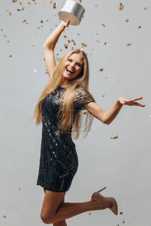 Photo for Merry Christmas: a Happy Blonde Woman in a Festive Dress Holding Christmas Presents With Confetti Flying All Around, a Portrait - stock photo - Royalty Free Image