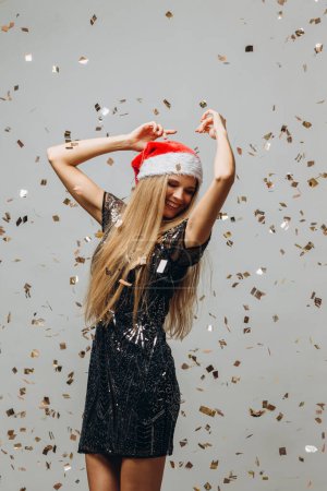 Photo for Beautiful blonde Santa girl dancing under glittering confetti. New Year party concept. - Royalty Free Image