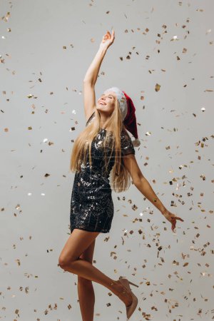 Téléchargez les photos : Belle blonde Santa girl dansant sous des confettis scintillants. Concept de fête Nouvel An. - en image libre de droit