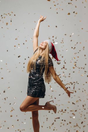 Foto de Hermosa rubia Santa niña bailando bajo confeti brillante. concepto de fiesta de Año Nuevo. - Imagen libre de derechos