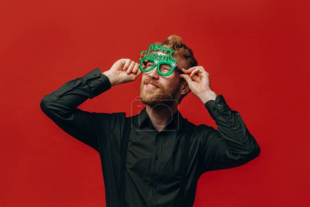 Téléchargez les photos : Charmant homme aux cheveux roux en lunettes de carnaval à la fête du Nouvel An. Studio photo. - en image libre de droit