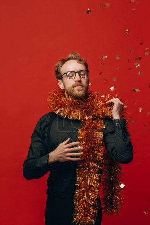 Foto de Hombre alegre pelirrojo en gafas y boa de oro en la fiesta de Año Nuevo con confeti. Estudio foto. - Imagen libre de derechos