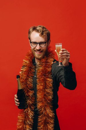 Foto de Hombre guapo de pelo rojo en copas y una boa dorada levanta una copa de champán. Celebración del nuevo año. - Imagen libre de derechos