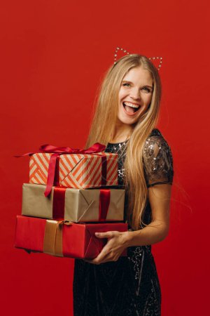 Téléchargez les photos : Joyeux Noël : une femme blonde heureuse dans une robe de fête tenant des cadeaux de Noël. Portrait - photo de la réserve - en image libre de droit