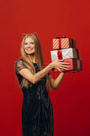Téléchargez les photos : Joyeux Noël : une femme blonde heureuse dans une robe de fête tenant des cadeaux de Noël. Portrait - photo de la réserve - en image libre de droit