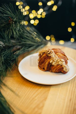 Photo for A delicious croissant on a table in a coffee shop decorated with festive Christmas lights. - Royalty Free Image