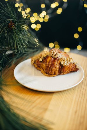 Téléchargez les photos : Un délicieux croissant sur une table dans un café décoré de lumières de Noël festives. - en image libre de droit