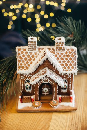 Téléchargez les photos : Petite maison en pain d'épice avec glaçure debout sur la table. Salon avec lumières et sapin de Noël. Humeur de vacances - en image libre de droit