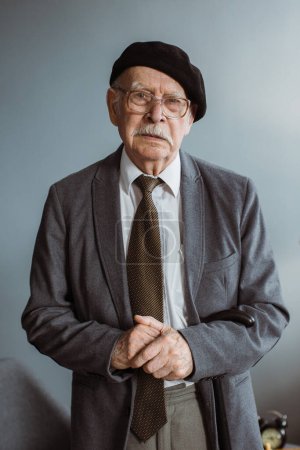 Téléchargez les photos : Portrait d'un homme âgé aux cheveux gris en lunettes debout dans le salon à la maison. - en image libre de droit