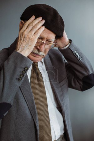 Téléchargez les photos : Homme aux cheveux gris dans les années 80 met un chapeau tout en se tenant dans le salon à la maison. - en image libre de droit