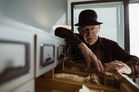 Photo for Senior male archivist searching for catalogs - Royalty Free Image