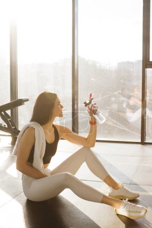 Téléchargez les photos : Relaxing after training. beautiful young woman looking away while sitting at gym and drink water. Young female at gym taking a break from workout. - en image libre de droit