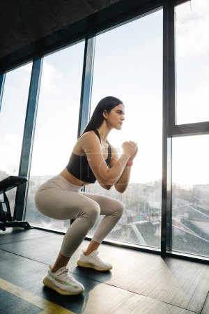 Foto de Athletic girl in sportswear, white leggings and black top doing squats in the gym. - Imagen libre de derechos