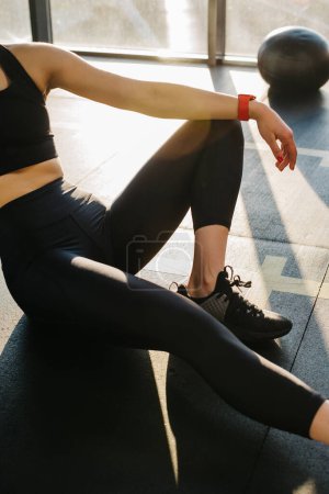 Téléchargez les photos : Close-up, athletic girl in black leggings sitting on the floor in the gym. Resting after exercise, leggings mockup. - en image libre de droit