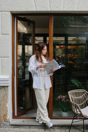 Téléchargez les photos : Magazine or book image mockup. A young hipster girl reads a magazine against the background of a cozy coffee shop. - en image libre de droit