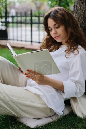 Téléchargez les photos : Magazine or book image mockup. The girl relaxes on the lawn in the courtyard of the coffee shop, reads a book. - en image libre de droit