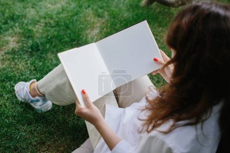 Photo for Magazine or book image mockup. The girl relaxes on the lawn in the courtyard of the coffee shop, reads a book. - Royalty Free Image