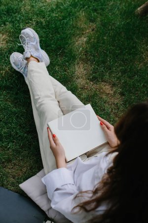 Foto de Magazine or book image mockup. The girl relaxes on the lawn in the courtyard of the coffee shop, reads a book. - Imagen libre de derechos