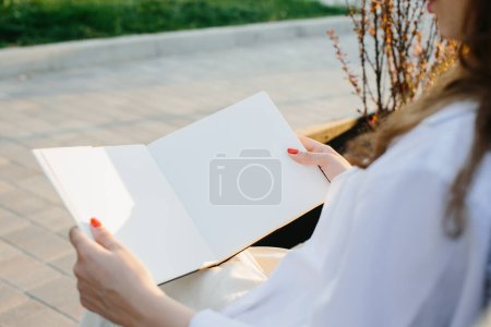 Photo for Magazine or book image mockup. A girl reads a book sitting on a bench on a city street at sunset. - Royalty Free Image