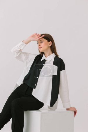Photo for Photo of a pretty woman in a black and white shirt sitting on a white cube, isolated on a white background. Shirt mockup. - Royalty Free Image