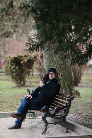 Téléchargez les photos : Un homme âgé profite d'une froide matinée d'hiver dans la ville. Un homme assis sur un banc sur la place, le concept de paix et de vitalité. - en image libre de droit