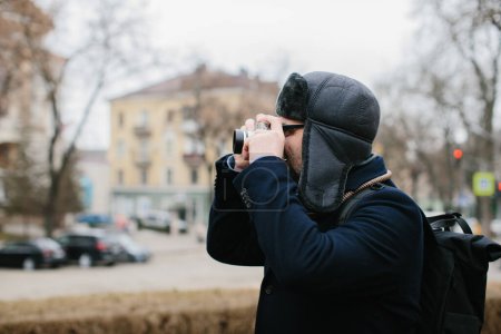 Téléchargez les photos : A senior tourist takes pictures of the winter city on his film camera. Travel and hobby concept. - en image libre de droit