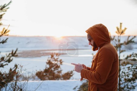 Photo for A hiker enjoys the sunset in the winter mountains and takes a photo on his phone. - Royalty Free Image