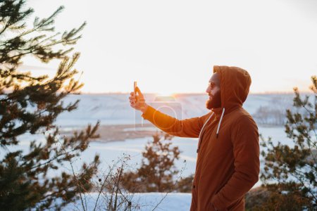 Téléchargez les photos : Un randonneur profite du coucher de soleil dans les montagnes d'hiver et prend une photo sur son téléphone. - en image libre de droit