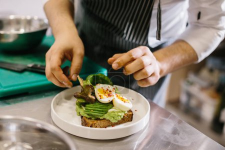Photo for The chef is preparing food. Close-up of a male chef preparing avocado toast in a spacious modern kitchen. - Royalty Free Image
