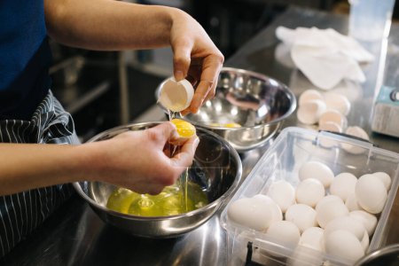 Foto de De cerca. Un cocinero en la cocina de un café o panadería. Las manos hembras rompen huevos para masa. - Imagen libre de derechos