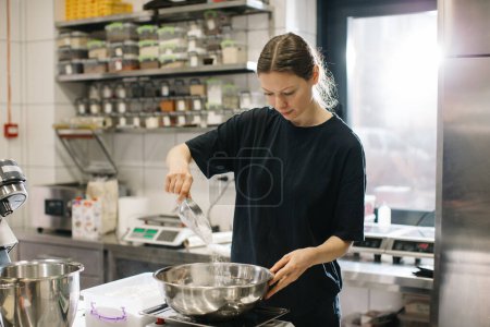 Téléchargez les photos : Une cuisinière travaille dans une cuisine industrielle moderne. Le processus de fabrication de gâteaux dans une boulangerie ou un café. - en image libre de droit