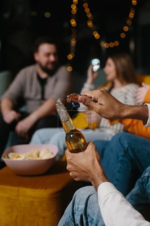 Foto de Abriendo una botella de cerveza de cerca. Un grupo de amigos se divierte viendo una película en un café. - Imagen libre de derechos